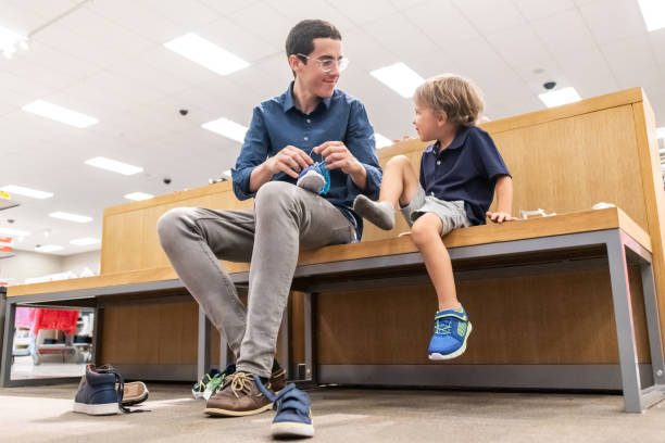 young man shopping for shoes for his son young man shopping for shoes for his son sitting in a department store bench shoe store stock pictures, royalty-free photos & images