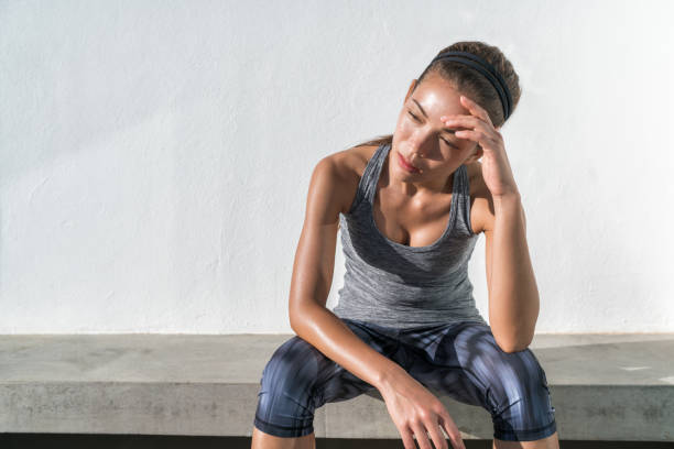 Tired fitness running woman sweating exhausted Tired fitness running woman sweating taking a break of cardio workout difficult training. Exhausted runner sitting with headache feeling exhaustion and dehydration from working out at outdoor gym. heat stress stock pictures, royalty-free photos & images