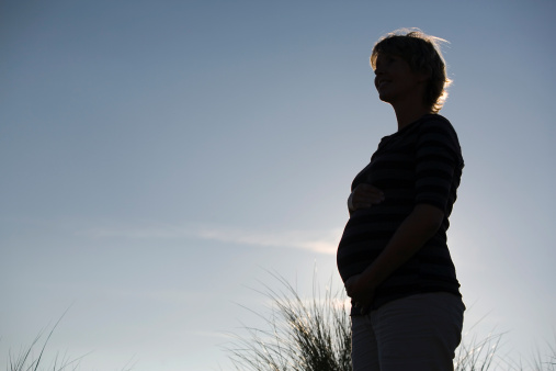 silhouette of a pregnant woman against a blue sky and holding her hands on her belly