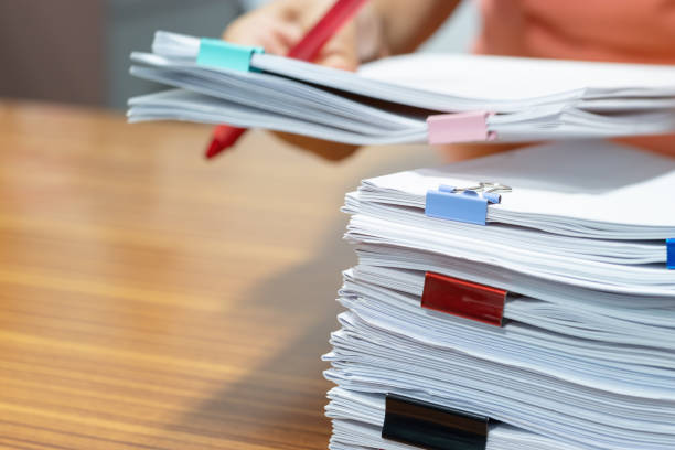 istock Teacher hand searching report papers and students homework assignment for checking score. Pile of unfinished paperwork stacked in archive with colorful paper clips. Business and education concept. 1160513394
