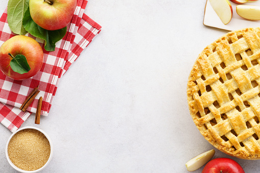 Homemade apple pie with lattice top and ingredients on gray table. Traditional American seasonal pastry background. Copy space.