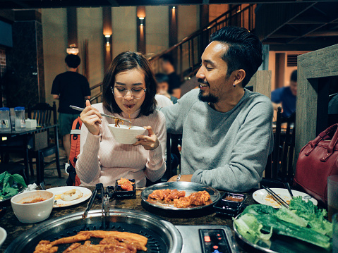 Hipster man and young asian woman eating Korean BBQ in the restaurant. Warm family, Father and daughter relationship