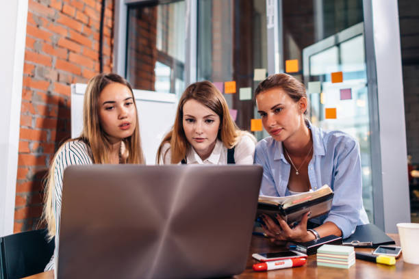 istock Three female college students studying together using laptop and lecture notes sitting at desk in study room 1160533699