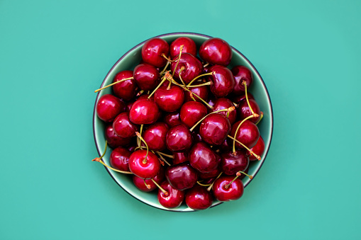 Fresh cherries in a bowl on green background. Summer healthy food concept.