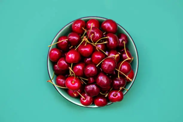 Photo of Fresh cherries in a bowl on green background. Healthy food concept