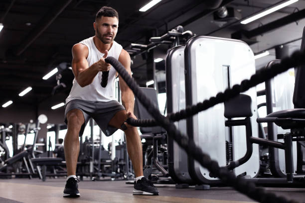 istock Athletic young man with battle rope doing exercise in functional training fitness gym. 1160537330