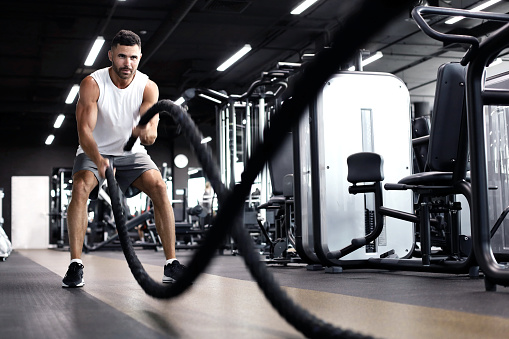 Athletic young man with battle rope doing exercise in functional training fitness gym