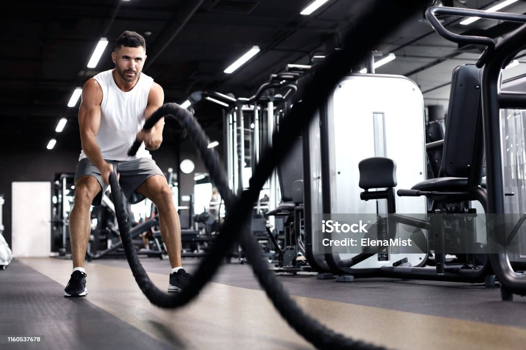Athletic young man with battle rope doing exercise in functional training fitness gym. Athletic young man with battle rope doing exercise in functional training fitness gym Rope Stock Photo