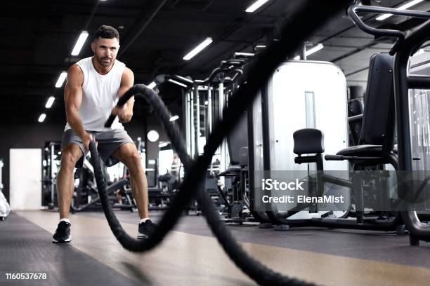 Athletic Young Man With Battle Rope Doing Exercise In Functional Training Fitness Gym Stock Photo - Download Image Now