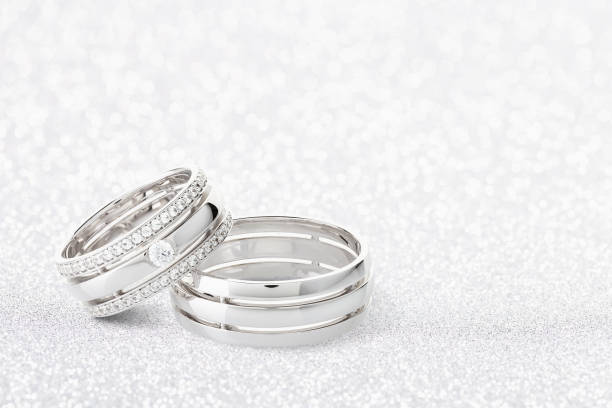 istock Pair of silver wedding rings with diamonds on white glossy background with bokeh 1160543809