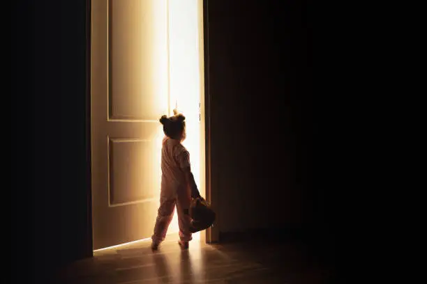 Photo of Little girl opens the door to the light in darkness