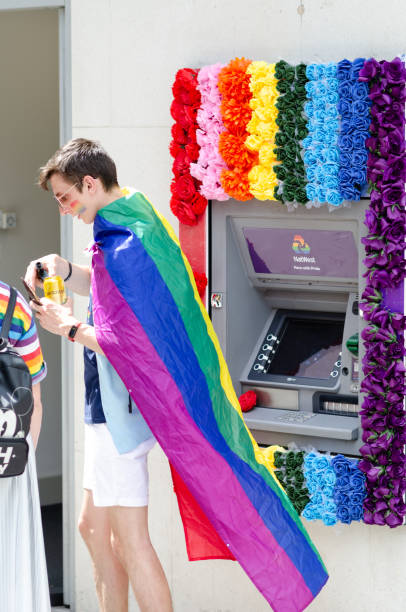 London Gay Pride parade 2019. LGBT supporter next to cash machine of one of the UK banks which is decorated in rainbow colours. stock photo