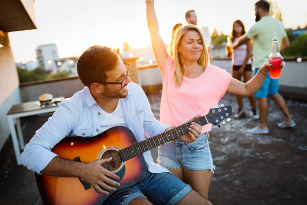 istock Young friends having fun at a rooftop party, playing the guitar, singing, dancing and drinking 1160549186