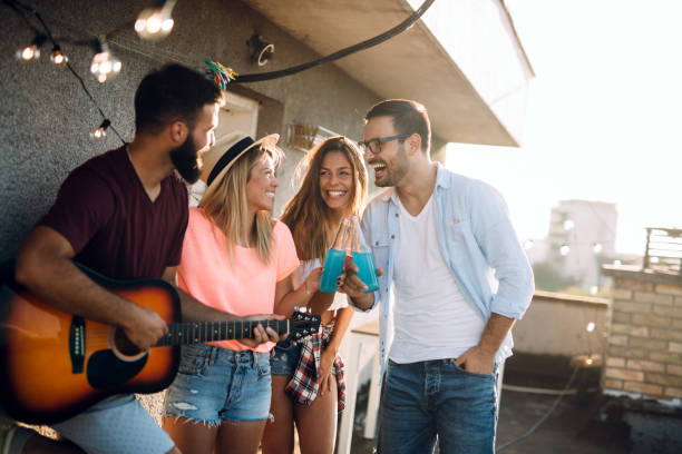 istock Young friends having fun at a rooftop party, playing the guitar, singing, dancing and drinking 1160549628