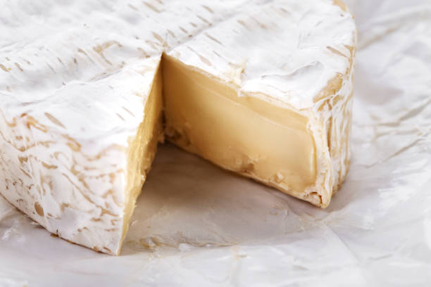 sliced round brie cheese head with white mold on white paper