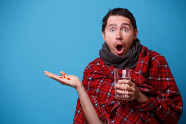 istock A wrapped in a blanket sick man with tablets and mug in his hands. 1160551687