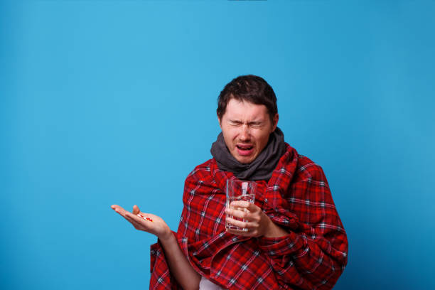 istock A wrapped in a blanket sick man with tablets and mug in his hands. 1160551706
