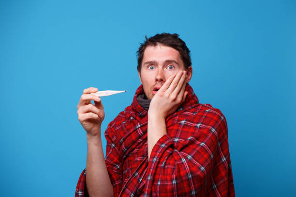 istock A sick man wrapped in a blanket is standing with a thermometer in his hands. 1160551724