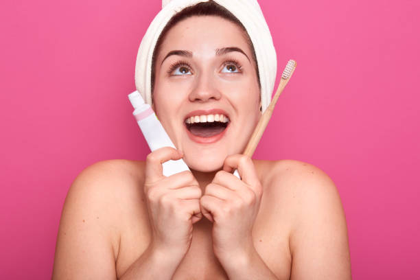 istock Young female with white towel on head an d nacked shoulders, ready for brushing teeth, looking up with open mouth and happy facial expression. Healthy lifestyle and motning procedures concept. 1160555375