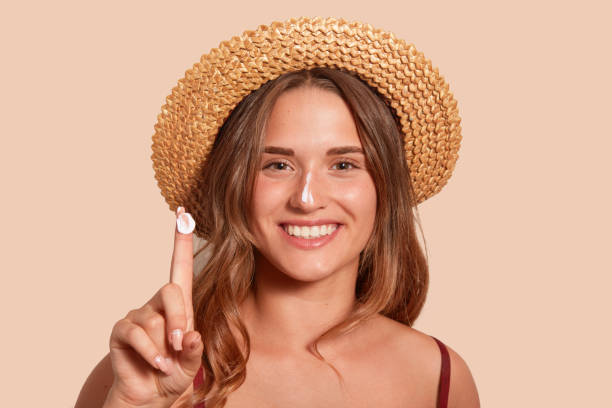 jeune femme applaying crème solaire sur son visage, et showinig son doigt avec la protection solaire, modèle posant isolé au-dessus du fond beige, restant contre le mur de studio avec le sourire de topothy, costume de natation habillé. - crème solaire photos et images de collection