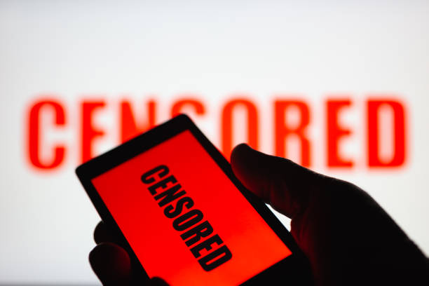 A smartphone in hand displaying the "censored" text. Same text in red blurred on white background. The concept of censorship on popular social networks. Restricted access to internet. Shallow DOF A smartphone in hand displaying the "censored" text. Same text in red blurred on white background. The concept of censorship on popular social networks. Restricted access to internet. Shallow DOF censorship stock pictures, royalty-free photos & images