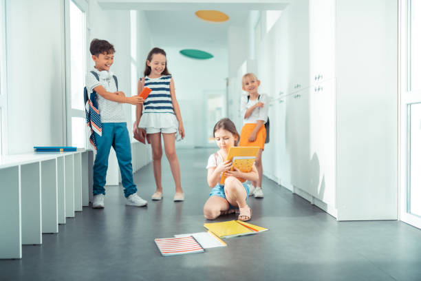 istock Poor girl picking up her books after boy pushed her 1160570049