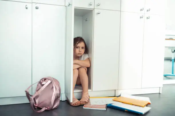 Lonely at school. Dark-eyed little scared girl sitting in the locker feeling lonely at school