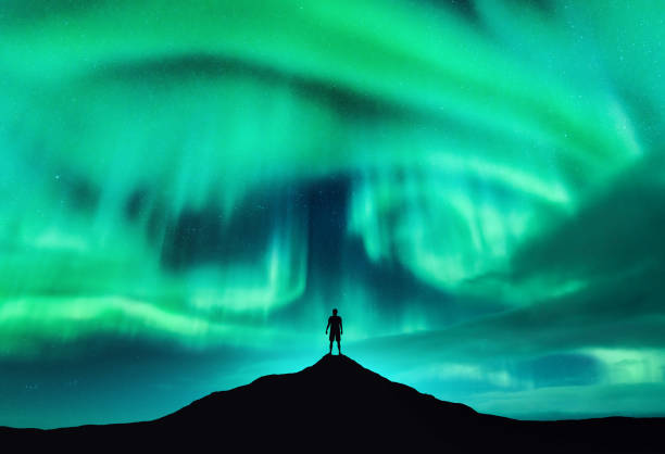 オーロラボレアリスと山頂の男のシルエット。ノルウェー、ロフォーテン諸島。美しいオーロラと男一人旅。星と極光の空。オーロラのある夜景 - 北極光 ストックフォトと画像