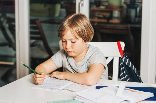 istock Cute little boy doing homework for school, writing in excersice notebook 1160571008