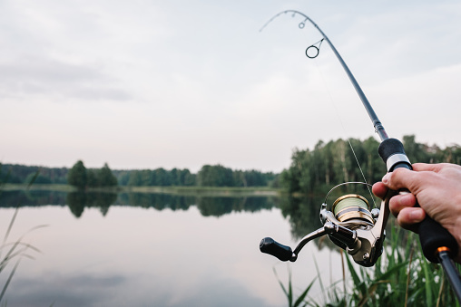 Fisherman with rod, spinning reel on the river bank. Fishing for pike, perch, carp. Fog against the backdrop of lake. background Misty morning. wild nature. Article about fishing day.