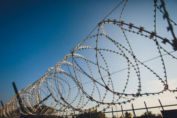 istock Coiled barbed wire fencing against a blue sky background. 1160574272