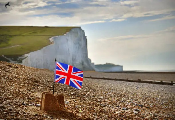 A sand castle on an English Channel beach flying a British Union Jack flag beneath symbolic White Cliffs
A British metaphor