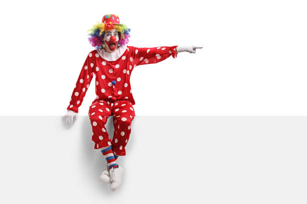 istock Clown sitting on a white panel and pointing to the side 1160584445