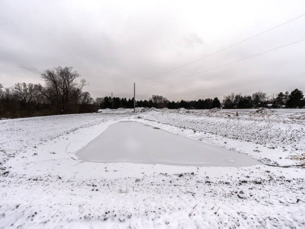 un homme gelé a fait l'étang de rétention couvert de glace et de neige blanche fraîche attendant le développement environnant de construction dans le wisconsin rural dans la saison d'hiver. - retention pond photos et images de collection