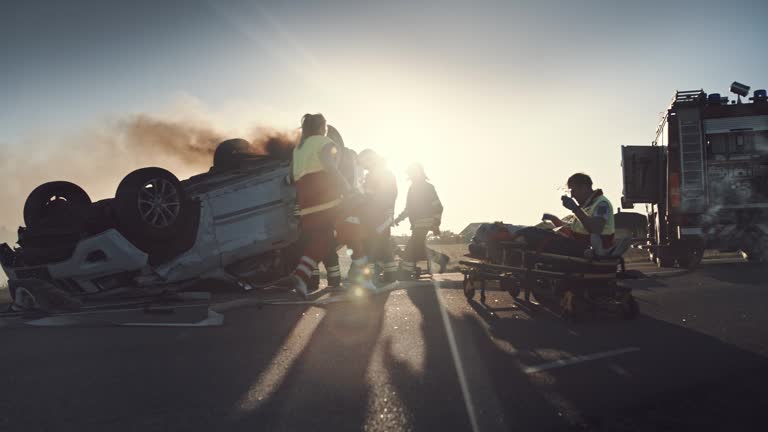 On the Car Crash Traffic Accident Scene: Paramedics Giving First Aid Oxygen Mask to Female Victim of the Accident. Firefighters Extinguish Fire and Use Hydraulic Cutter to Free Other Passengers