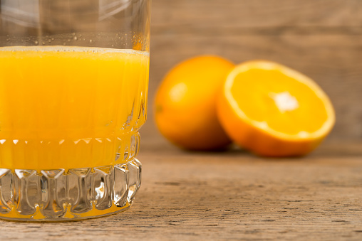 Glass of orange juice with half oranges on vintage table