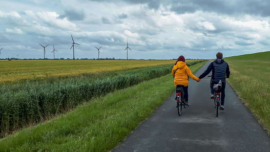 Young couple in love holding hands while cycling along the dike in Krummhörn, East Frisia, Northern Germany