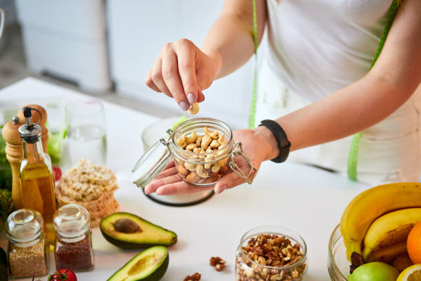 joven mujer feliz comiendo diferentes nueces (cashew, avellana, almendra) en la cocina moderna. concepto de alimentación saludable y dietética. pérdida de peso - nut fotografías e imágenes de stock