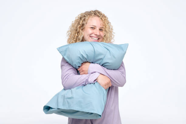 istock Cheerful curly blond woman in pajama hugging a pillow 1160601083