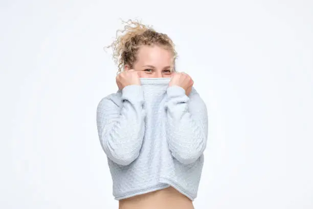 Photo of Curly blonde girl pulling sweater over head having fun being shy and childish