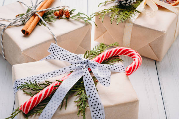 istock Gift boxes wrapped in wrapping paper with ribbons, pine cones and dried oranges on a white wooden background 1160604331