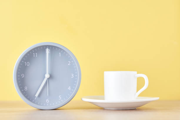 istock Classic gray alarm clock and white coffee cup on a yellow background 1160604379
