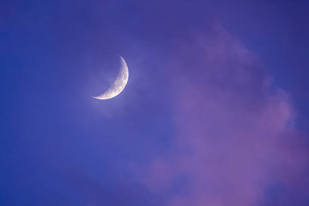 Crescent moon through purple sunset clouds stock photo
