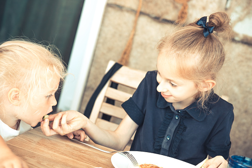 Happy elder sister feeding small sister in cafe restaurant concept for children care childhood lifestyle