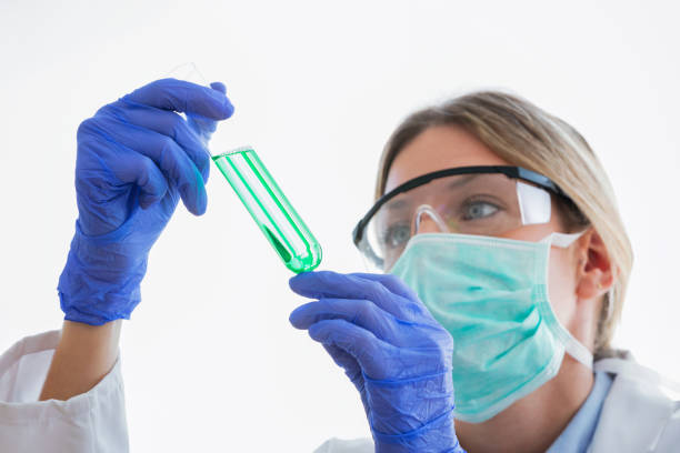 giovane scienziata donna con occhiali protettivi che guardano la provetta su sfondo bianco. - test tube biologist laboratory beaker foto e immagini stock