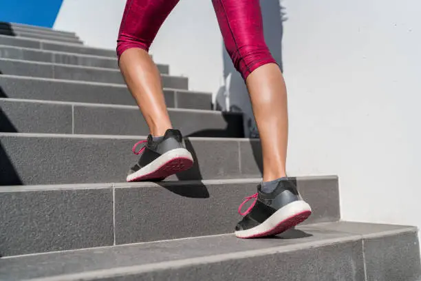 Stairs climbing running woman doing run up steps on staircase. Female runner athlete going up stairs in urban city doing cardio sport workout run outside during summer. Activewear leggings and shoes.