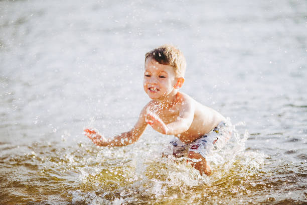 istock boy child playing makes splashes, beats hands on the water in the river at sunset 1160627263
