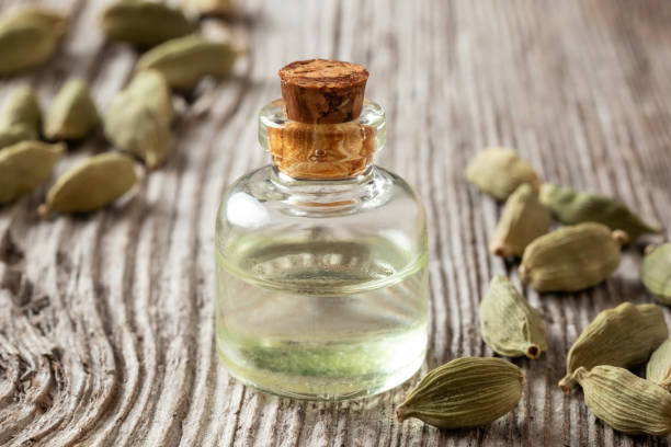 une bouteille d'huile essentielle de cardamon avec des graines entières de cardamon - huile essentielle de cardamone photos et images de collection