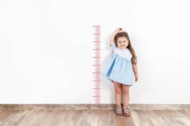 Little blond girl measuring height on white wall