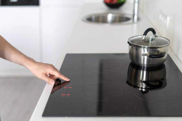 istock Woman using built in stove with saucepan on top, selecting program on display 1160634013
